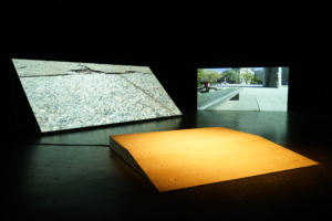 Installation of two screens and a wooden platform in a dark gallery