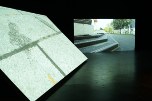 Installation of two screens and a wooden platform in a dark gallery