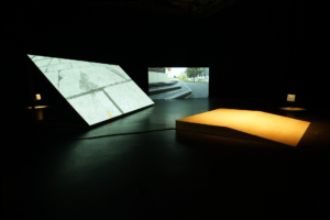 Installation of two screens and a wooden platform in a dark gallery