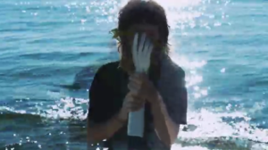 Still image from the video. A human standing in water holds an artifical hand in front of their face